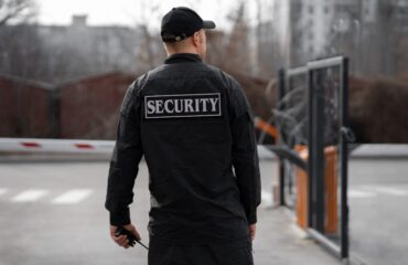 Rear view of a security guard on duty at a gated property in Vancouver, wearing a black uniform with 'Security' written on the back.