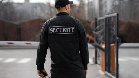 Rear view of a security guard on duty at a gated property in Vancouver, wearing a black uniform with 'Security' written on the back.