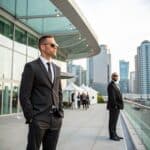 Professional security guards in formal attire overseeing a corporate event outdoors in a modern urban setting with a glass building backdrop in Vancouver.